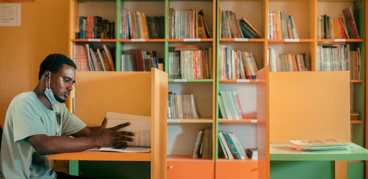 The Art of Drawing Readers In: Your attractive post title goes here Focused young man studying at a cubicle in a vibrant library, surrounded by books.